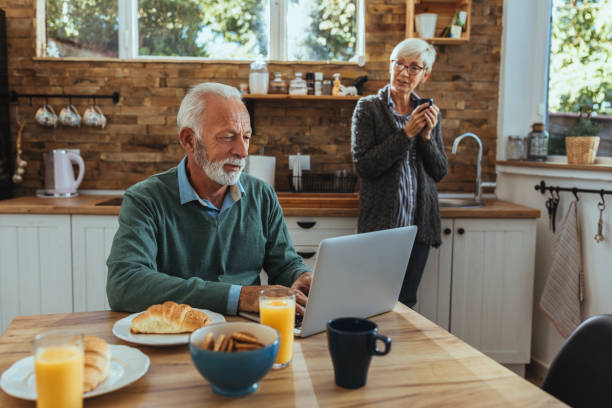 Mature couple enjoying morning at their kitchen and using technology
